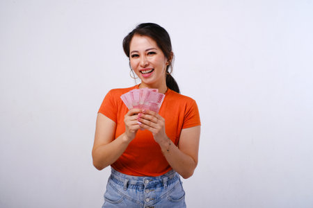 Smiling Asian woman wearing casualÂ shirt holding Indonesian money isolated on white backgroundの写真素材