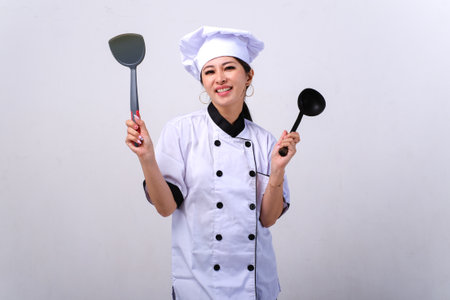 Portrait of a beautiful chef woman in uniform holding kitchen utensilsの写真素材
