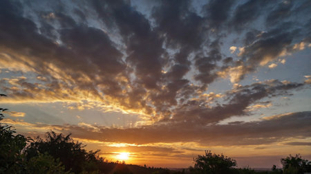 Sunset in the countryside with clouds and trees in the foreground.