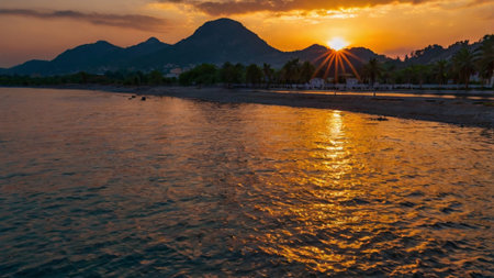 Sunset on the beach with palm trees and mountains in the backgroundの写真素材