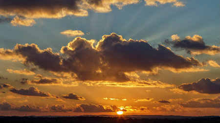 Sunset over a field with clouds in the sky. The sun's rays make their way through the clouds.の写真素材