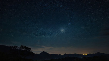 Milky way in the night sky with stars and silhouette of mountain.