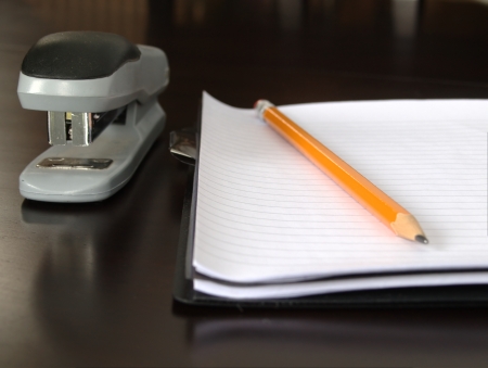 Notepad sitting on a desk with a pencil and staplerの写真素材
