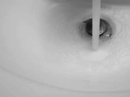 Water pouring into a white sink with a silver drain plug.