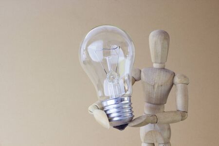 wooden person holds electric bulb in handの写真素材