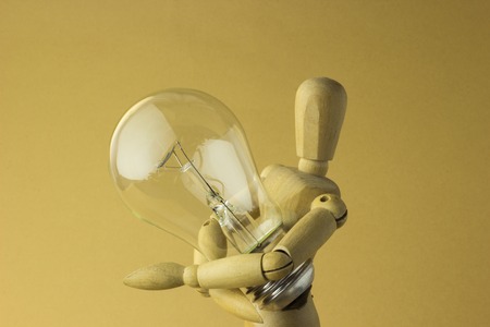 wooden person holds electric bulb in handの写真素材