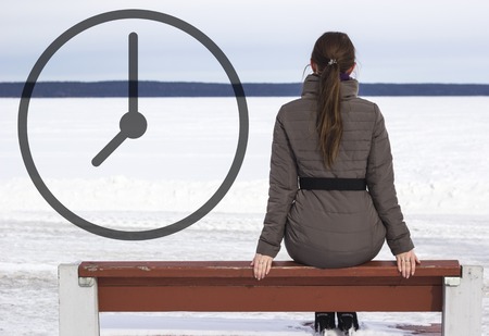 Rear view of a lonely young brunette woman sitting on a bench on the waterfrontの写真素材