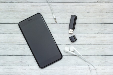 Smartphone with headphones and a flash drive on a wooden background, music storage concept