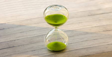 Hourglass with green sand on a wooden background