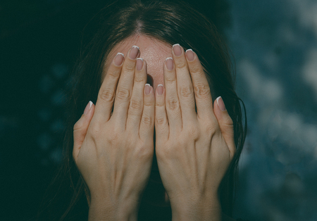 Girl covers her face with her hands, toned photoの写真素材