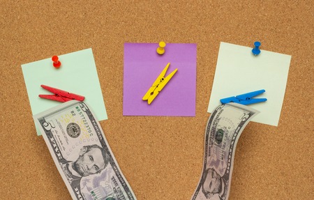 Three colorful notes with pushpins and clothespins with money isolated on a cork backgroundの写真素材