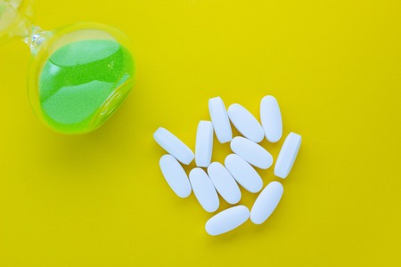 Hourglass with pills on a yellow background, concept time is healthの写真素材