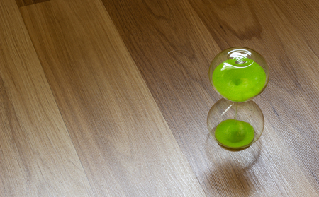 Hourglass with green sand on a wooden surface, top viewの写真素材