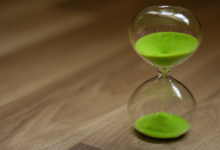 Hourglass with green sand on a wooden background