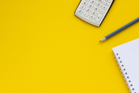 Calculator, notepad and pencil on a yellow background, space for textの写真素材
