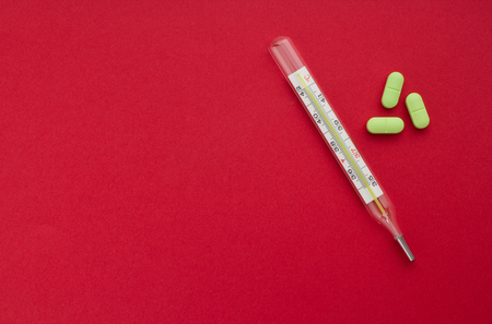 Mercury thermometer with tablets on a red background, concept of healthの写真素材