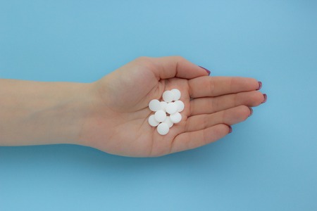 Female hand holding a white tablet on a blue background, concept of healthの写真素材