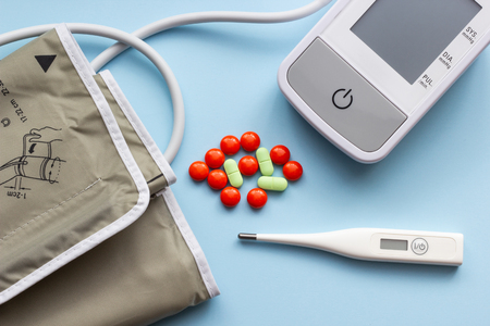 Electronic thermometer and tonometer with pills on a blue background, close-upの写真素材