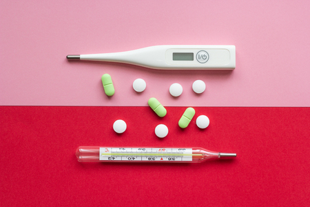 Thermometers on a pink and red background with white and green tabletsの写真素材