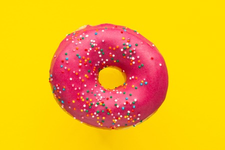 Donut pink with sprinkles isolated on yellow background, close-upの写真素材