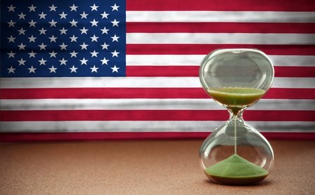 Sand running through the bulbs of an hourglass measuring the passing time in a countdown to a deadline, on USA flag background with copy spaceの写真素材
