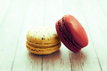 Yellow and red macaroons on wooden table with lightの写真素材