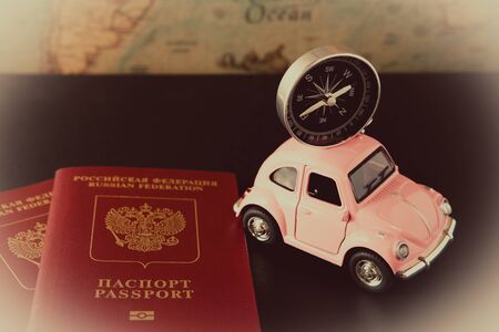 Small pink car with a compass on the roof and passports on a background of vintage maps, travel concept, view from aboveの写真素材
