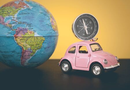 Pink retro car with world globe sphere on yellow background, toned photoの写真素材