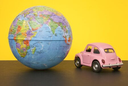 Pink little retro car with world globe sphere. Travel concept. Planning season vacations. Close-up.