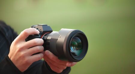 Photographer men shooting images. Man hands holding camera taking photos. Vivid blur green...