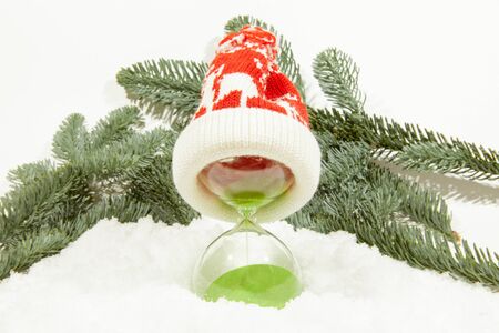 Hourglass in a Christmas hat, on the background of fir branches. The concept of the outgoing year and the arrival of the new year.の写真素材