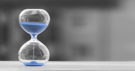 Hourglass with blue sand on a blurred black and white background, sand trending color