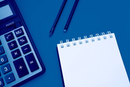 Notepad with two pencils and a calculator on a yellow background, toned trendy classic blue color of year 2020の写真素材
