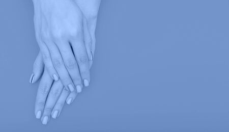 Stylish trendy female manicure. Beautiful young woman's hands on yellow background. Close-up, toned trendy classic blue color of year 2020の写真素材