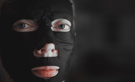 Close-up woman relaxing with a charcoal facial mask on dark background