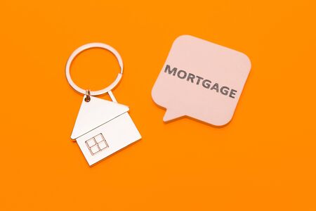 Mortgage concept. Metal keychain in the form of a house and a sticker with the inscription - mortgage on an orange background.の写真素材