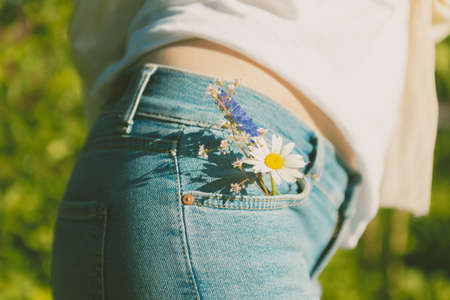 Close-up. Girl in blue jeans with flowers in her pocket on a background of nature.の写真素材
