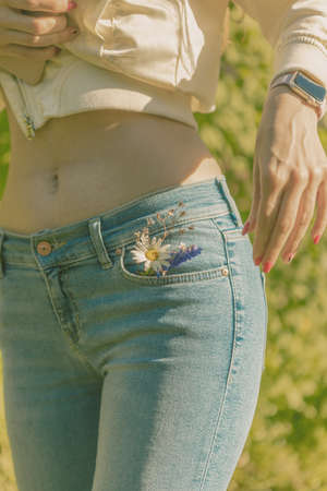 Beautiful girl in blue jeans with a camomile in her pocket. Walk in the green park.の写真素材