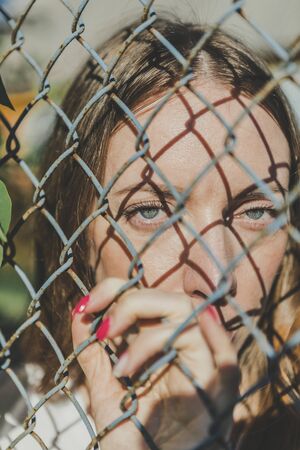 Close-up. The face of a young girl behind a metal fenceの写真素材