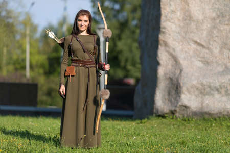 Woman with bow and arrow on the background of a large stone