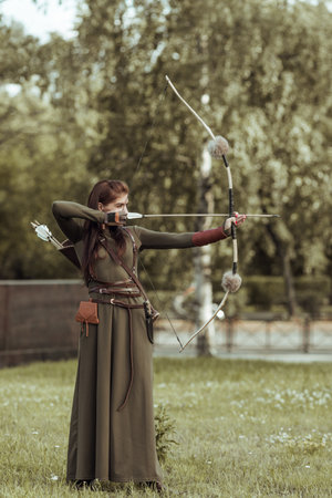 Young woman warrior with a bow pulls the bowstring with an arrow