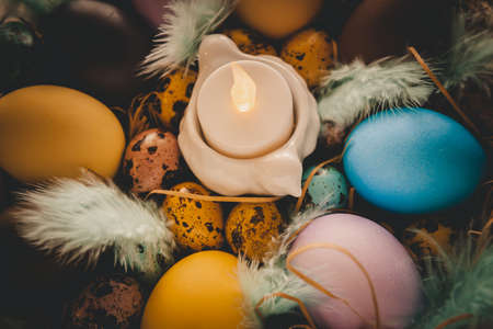 Colorful easter eggs with candle in basket on table