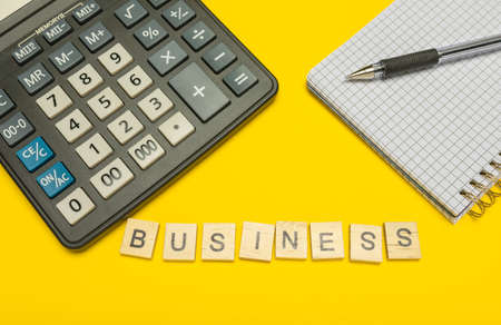 Word business made with wood letters and modern calculator with pen and notebook on yellowの写真素材