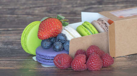 Close-up. Delicious different color macaroons and wild berries with strawberries on a wooden...