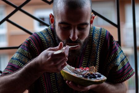Buddhist man eating healthy breakfast in papaya bowl. Yogurt in papaya bowl with granola, fresh strawberries, blueberries, coconut, chocolate, yogurt and chia seedsの写真素材