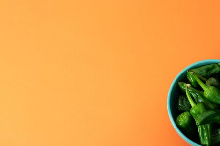 Plate with Padron peppers on orange background. Copy space