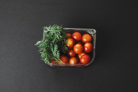 Cherry tomatoes in a plastic container on black backgroundの写真素材