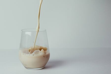Pouring coffee with milk into a transparent glass with ice cubes. White backgroundの写真素材