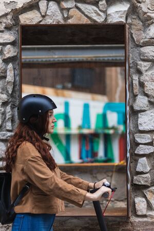 Pretty young woman with helmet riding electric scooter on the streetの写真素材