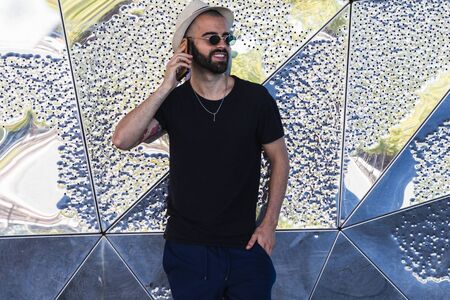 Smiling man in wattled hat smiling while making a call against of abstract wallの写真素材